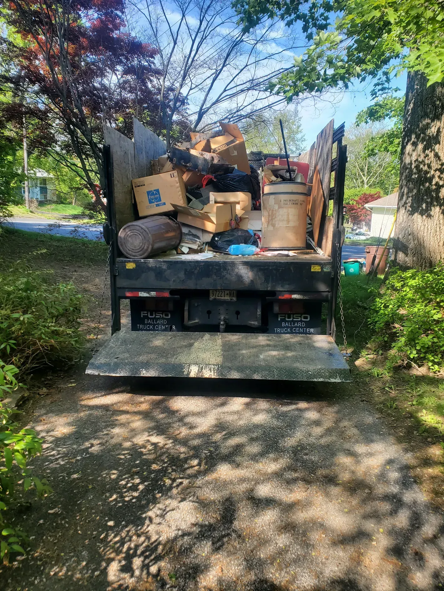 A dumpster truck filled with boxes and trash is parked on a dirt road.
