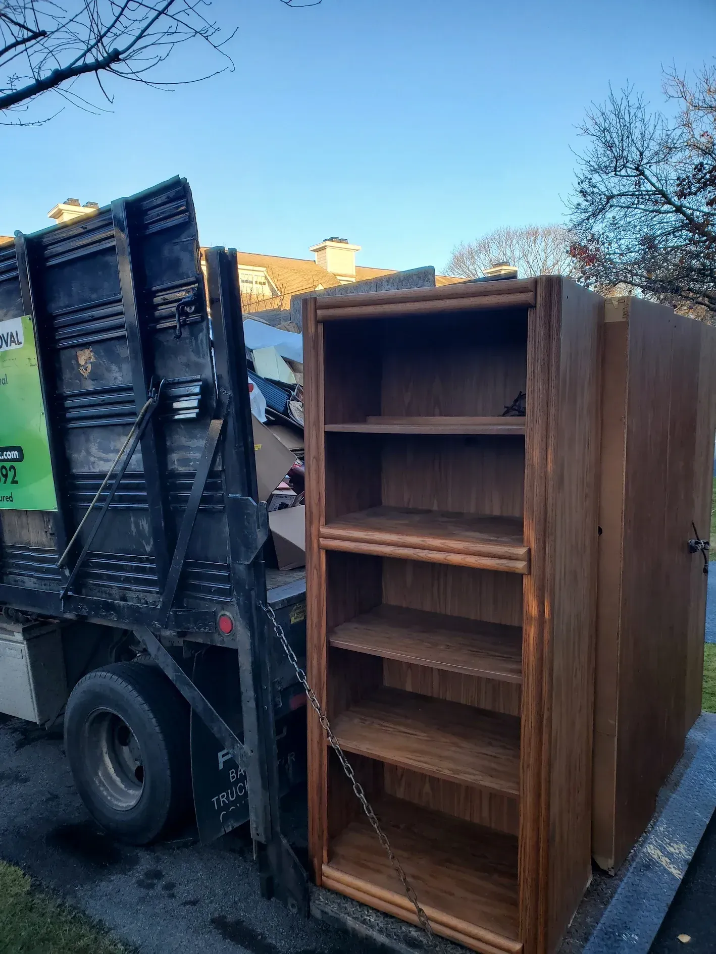 A garbage truck is carrying a wooden cabinet on a trailer.