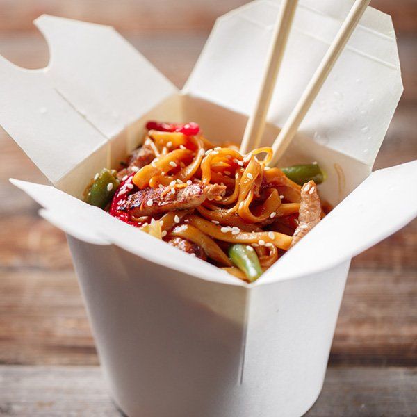 A take out box filled with noodles and chopsticks