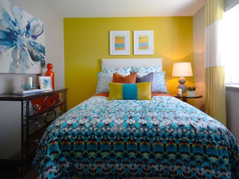 A bedroom with a bed , nightstand , lamp and yellow walls.