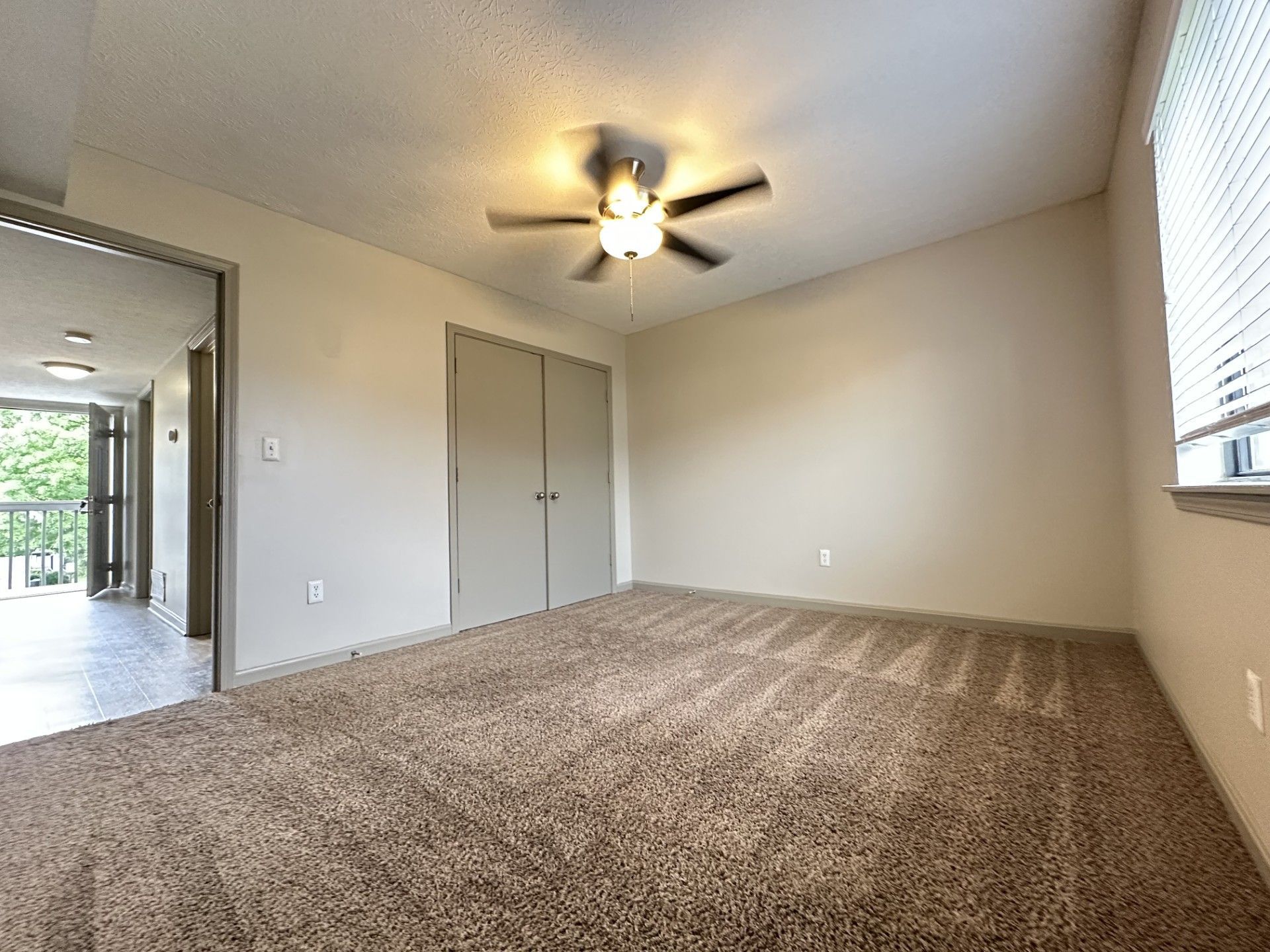 An empty room with a ceiling fan and a window.