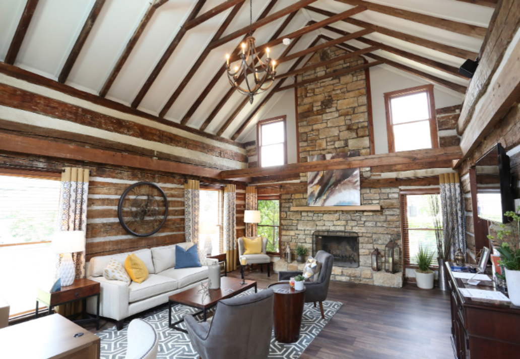 A living room in a log cabin with a couch , chairs , and a fireplace.
