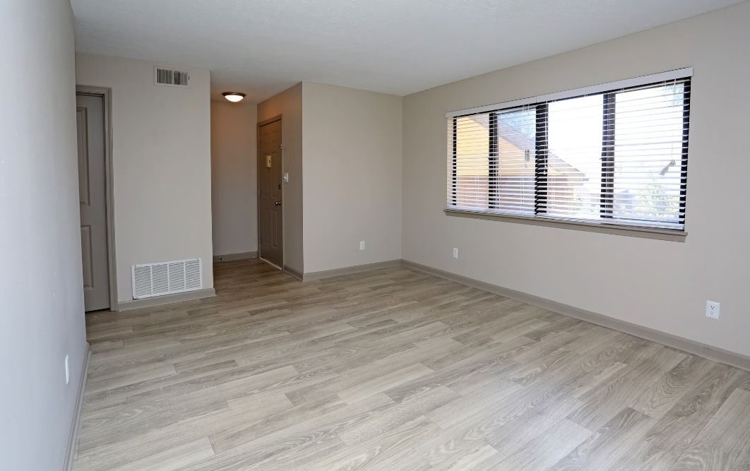 An empty living room with hardwood floors and a large window.
