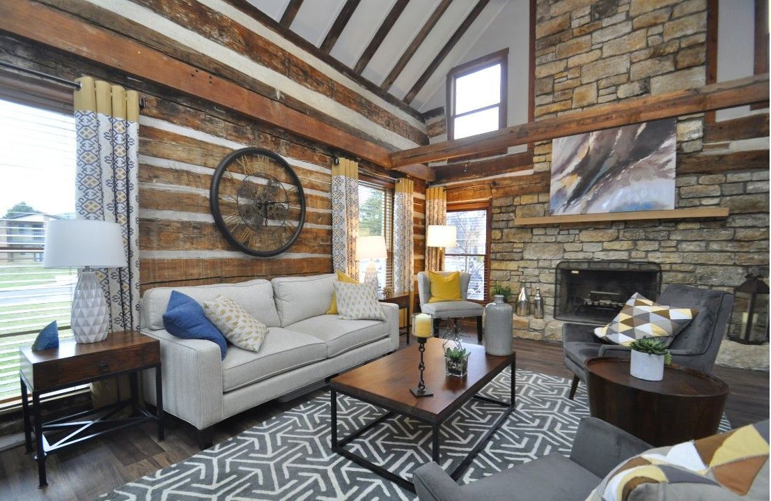 A living room in a log cabin with a couch , chairs , coffee table and fireplace.