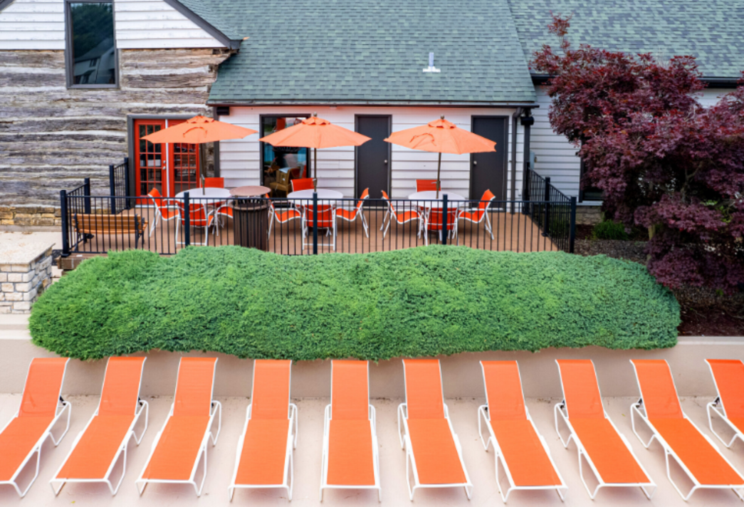 A row of orange lounge chairs and umbrellas in front of a house.