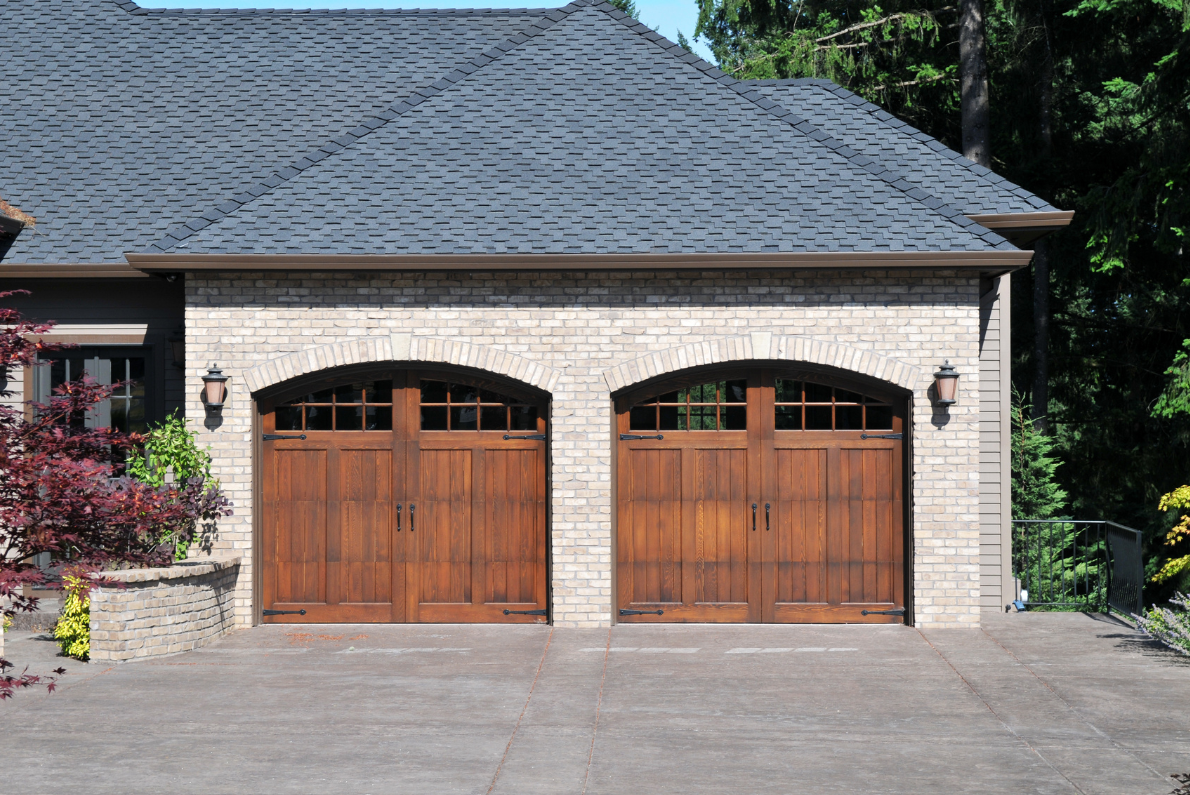 Two-car garage with arched wooden doors, brick facade, and dark gray shingled roof.