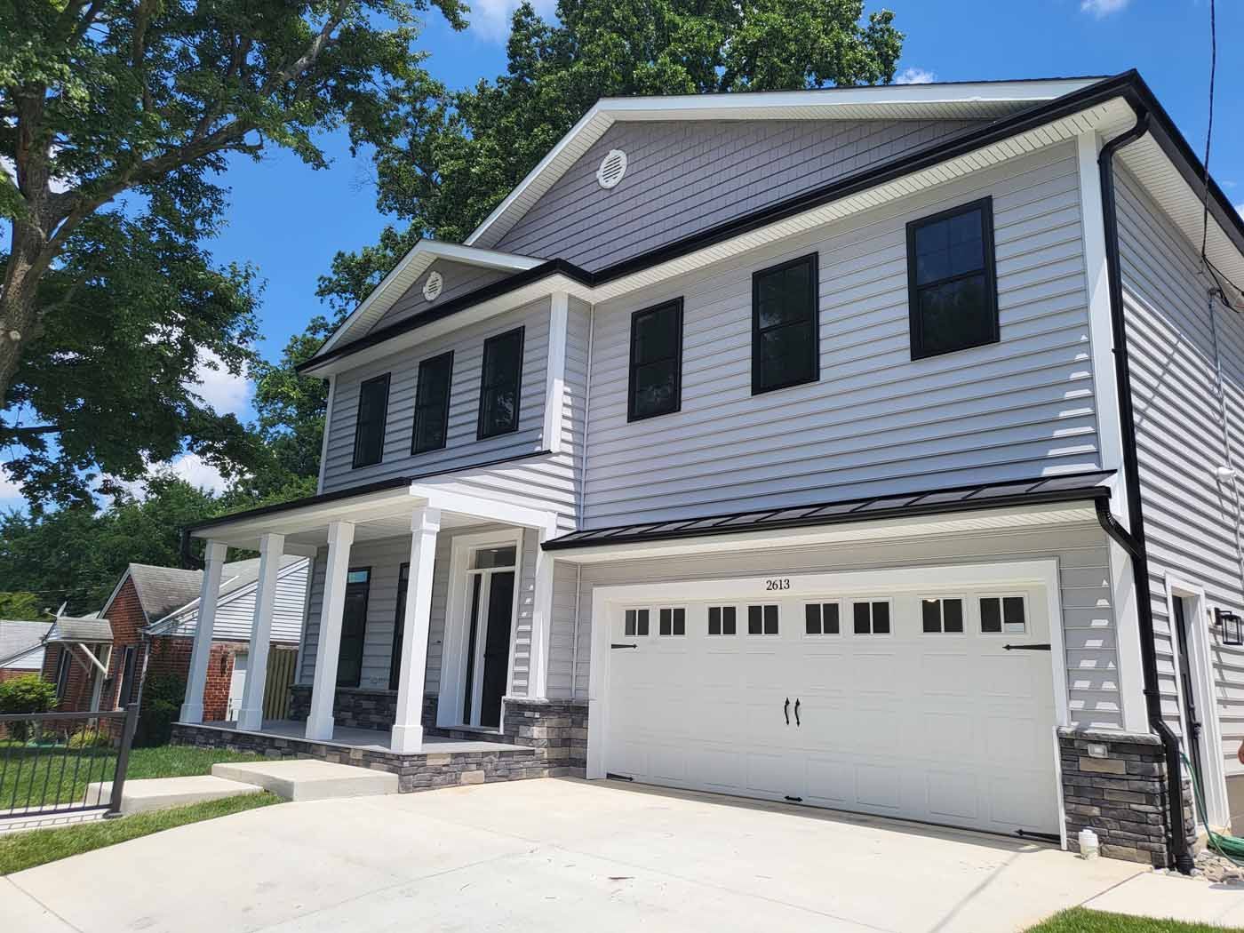 Two-story house with gray siding, white trim, and a white garage door, set against a blue sky.