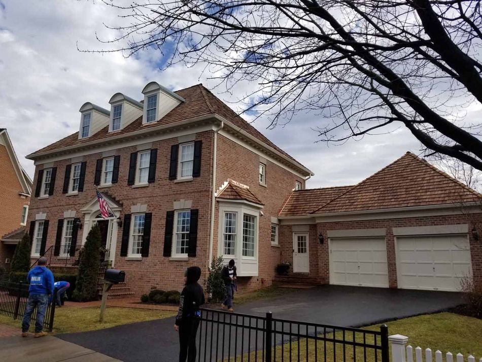 Two-story brick house with attached garage, black shutters, and three dormers. People near the front.