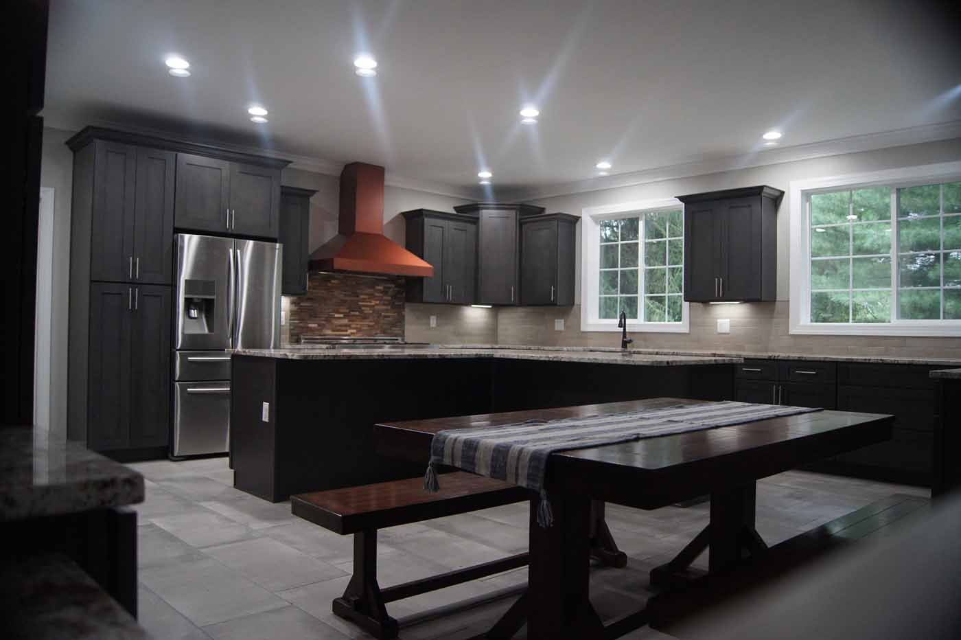 Dark-toned kitchen with brown cabinets, copper range hood, and a dark wooden dining table with a bench.
