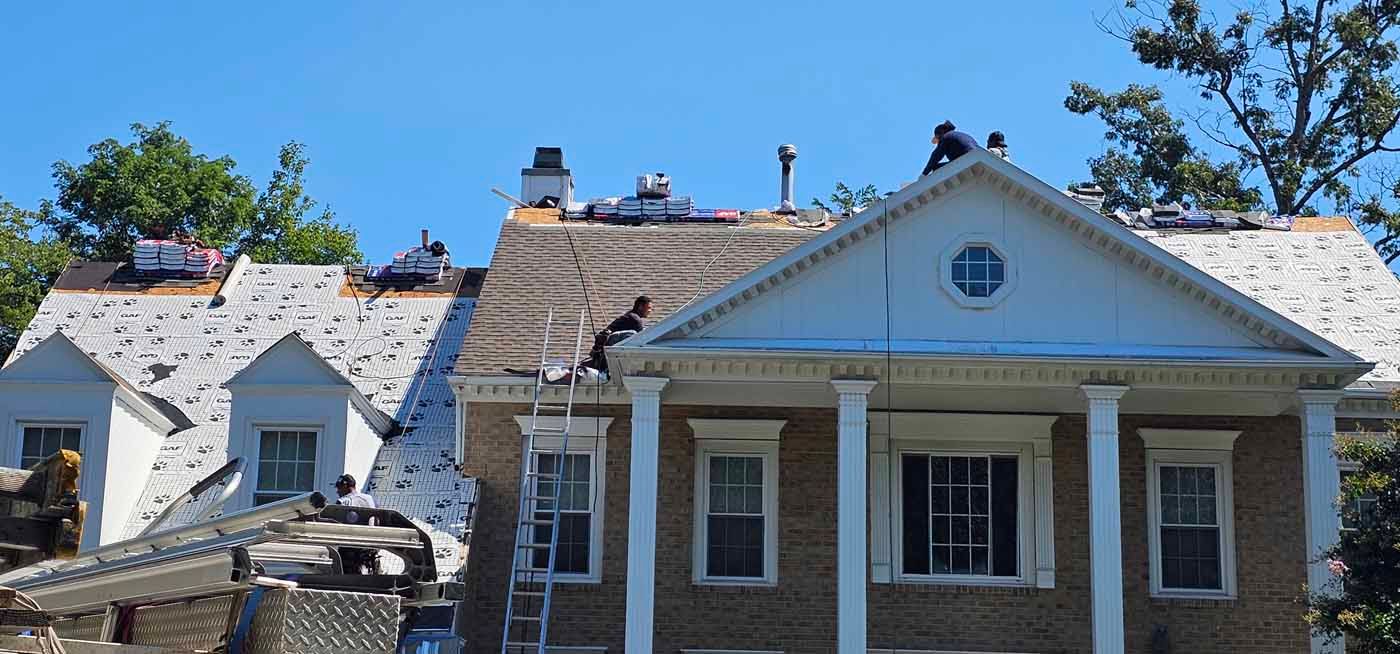 Roofers working on a house with white columns. The roof is partially torn off with materials stacked on top.
