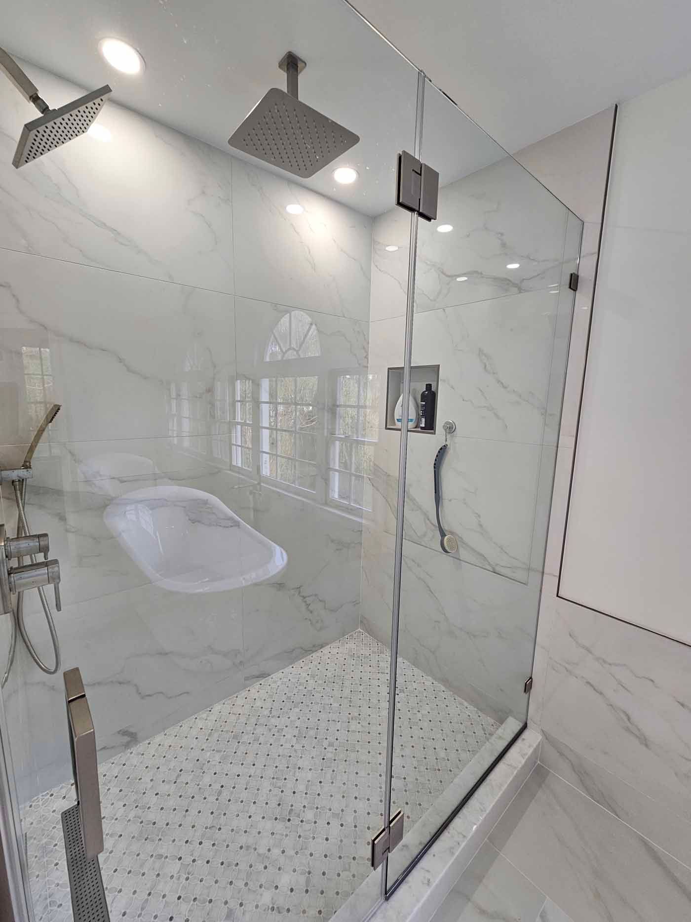 Modern walk-in shower with glass doors, marble tile walls, and mosaic tile floor. Two showerheads and chrome fixtures.
