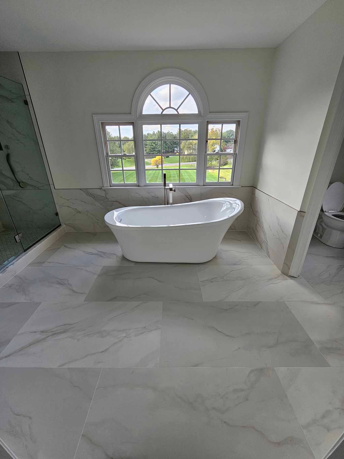 Spacious white bathroom with a freestanding tub, large window, and light-colored tile flooring.