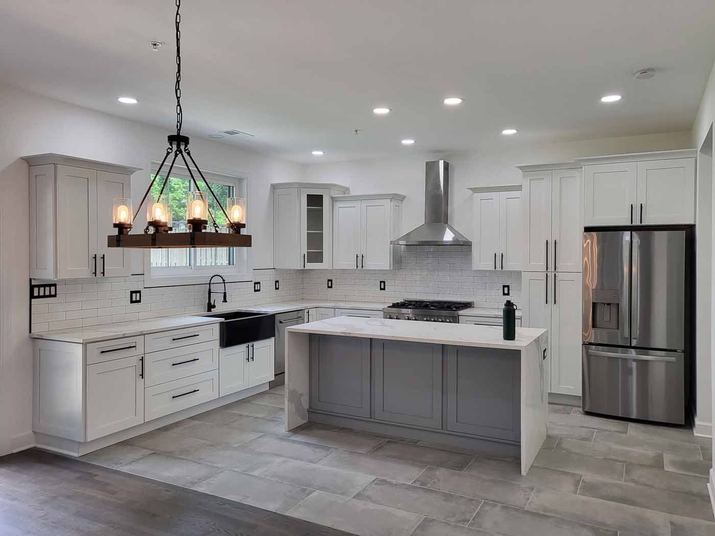 Modern kitchen with white cabinets, gray island, stainless steel appliances, and tile floor.