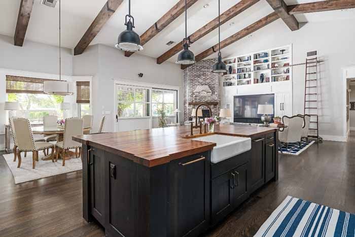 Kitchen with dark wood island, wooden beams, dining area, and fireplace with built-ins.