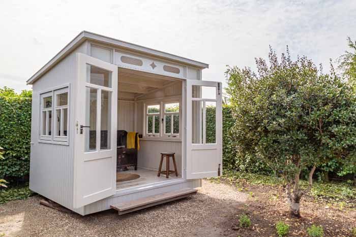 A small, light-colored garden shed with open double doors and windows, set in a yard.