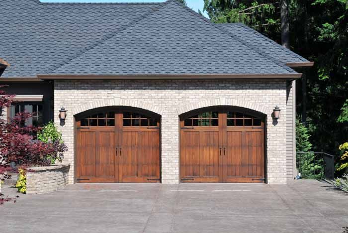 Double garage with arched wooden doors, light brick facade, and gray shingled roof.