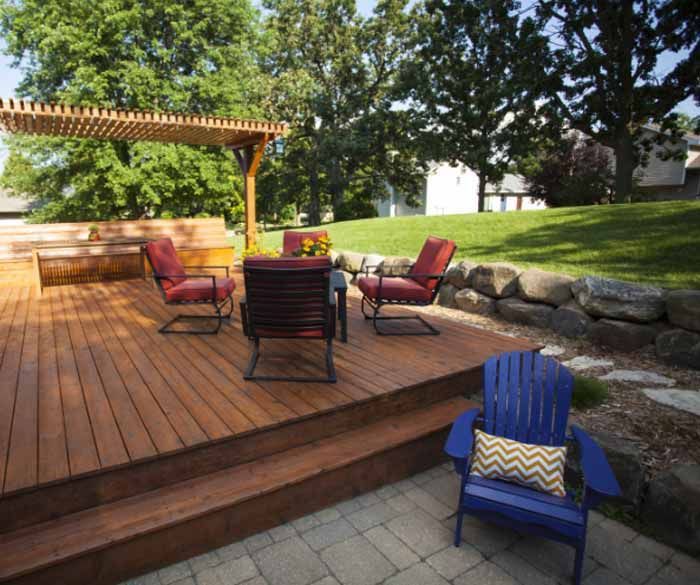 Wooden deck with patio furniture, pergola, and sloped green lawn in a backyard setting.