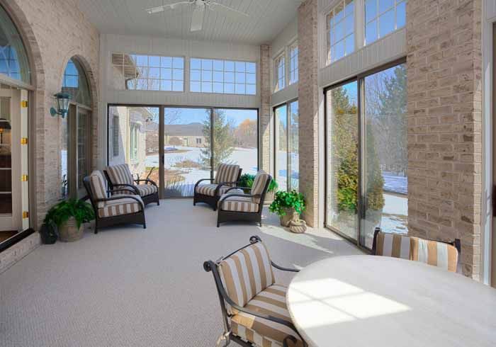 Sunroom with brick walls, large windows, and outdoor furniture. Snowy landscape visible outside.