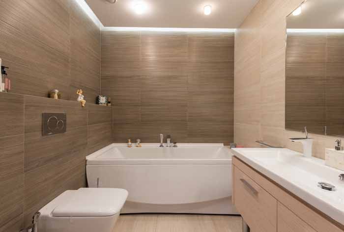 Modern bathroom with a white bathtub, toilet, and vanity against brown tiled walls.