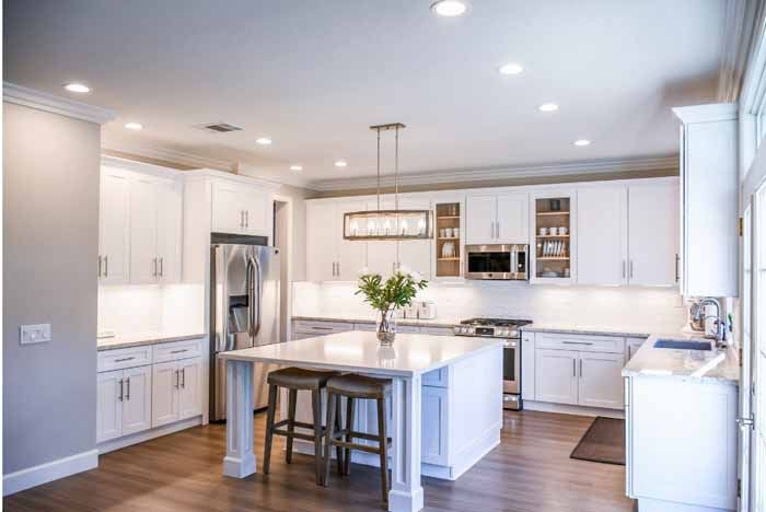 Bright white kitchen with island, stainless steel appliances, and wooden floors.