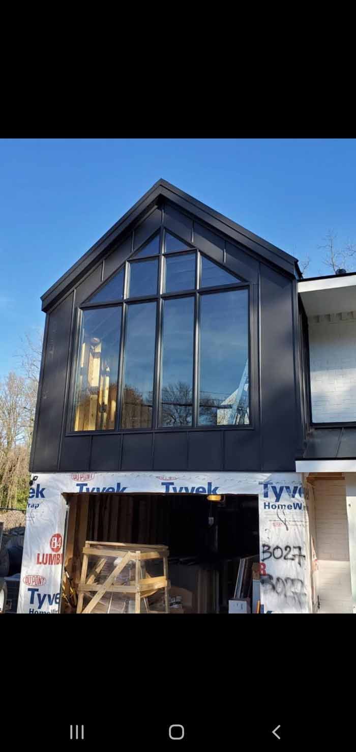 Black-sided building with large window and open garage. Blue sky. Construction wrap visible.
