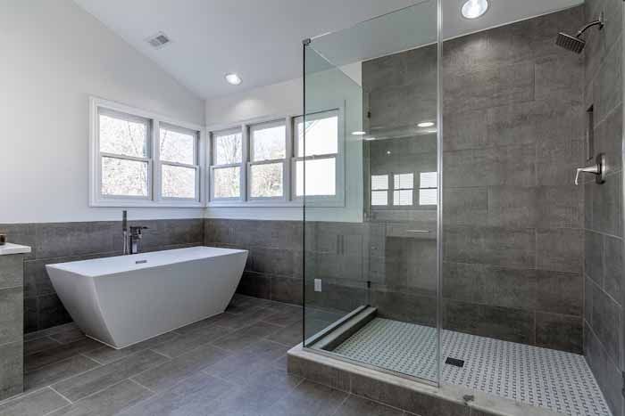 Modern bathroom with a white tub, walk-in shower, and gray tiled walls and floor.