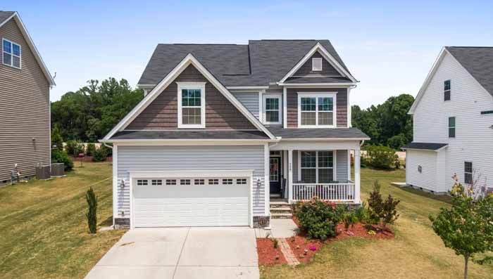 Two-story house with light blue siding, brown accents, white garage door, small porch, and manicured lawn.