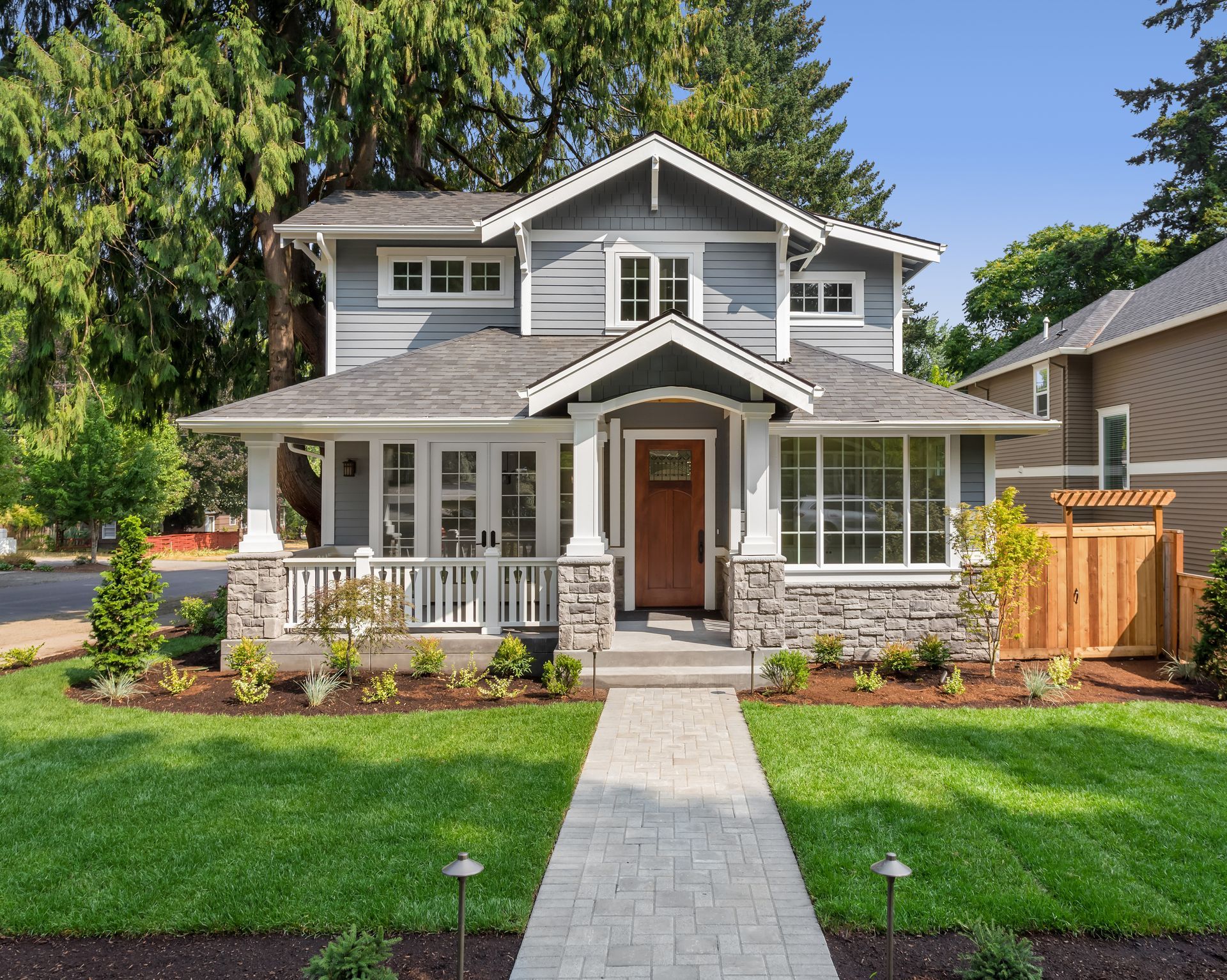 Gray craftsman-style house with stone accents, a porch, and a walkway leading to the front door.