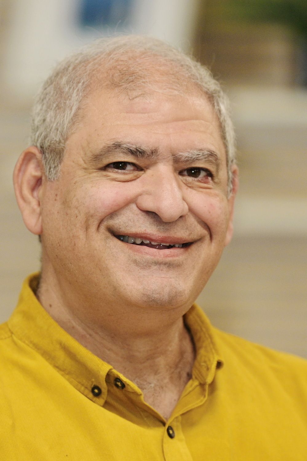 גבר בחולצה צהובה מחייך למצלמה.