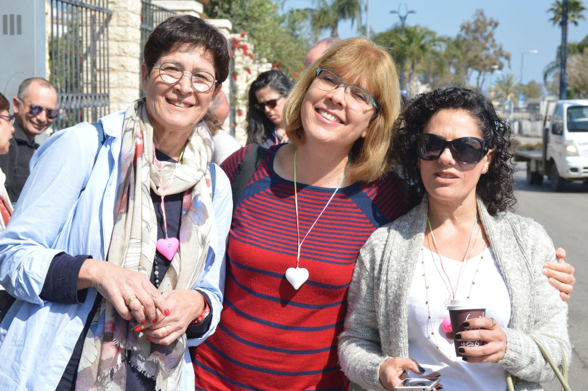 שלוש נשים מצטלמות יחד ברחוב.