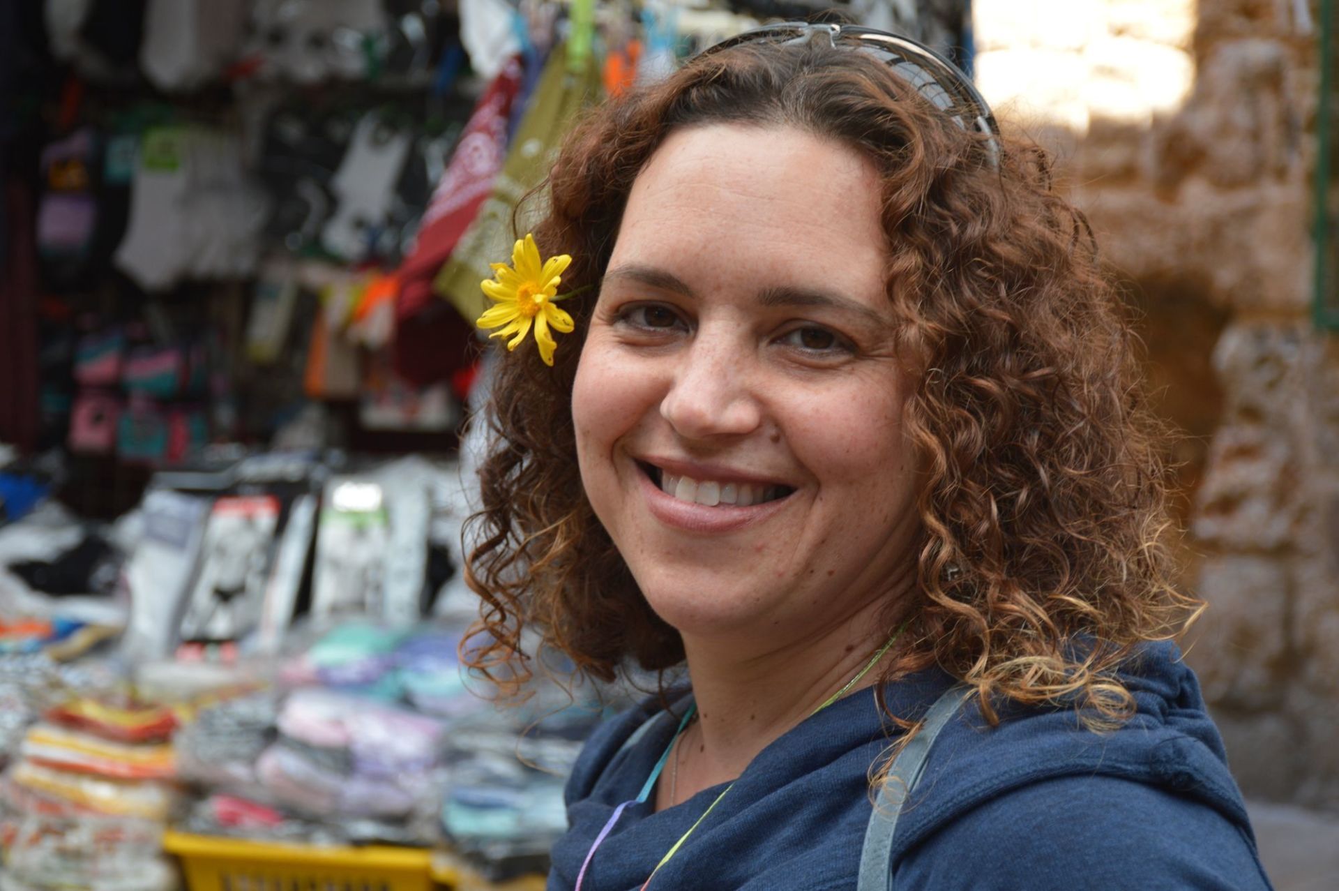 אישה עם שיער מתולתל מחייכת עם פרח צהוב בשערה.