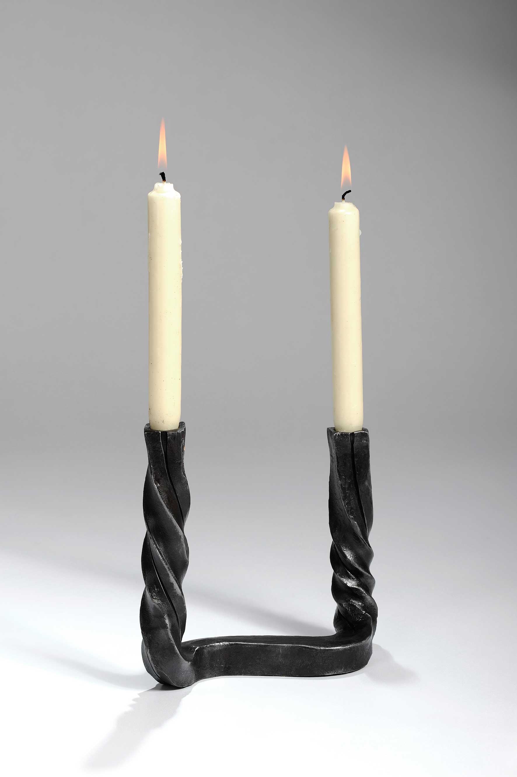 שני נרות דולקים בפמוט שחור על משטח לבן.