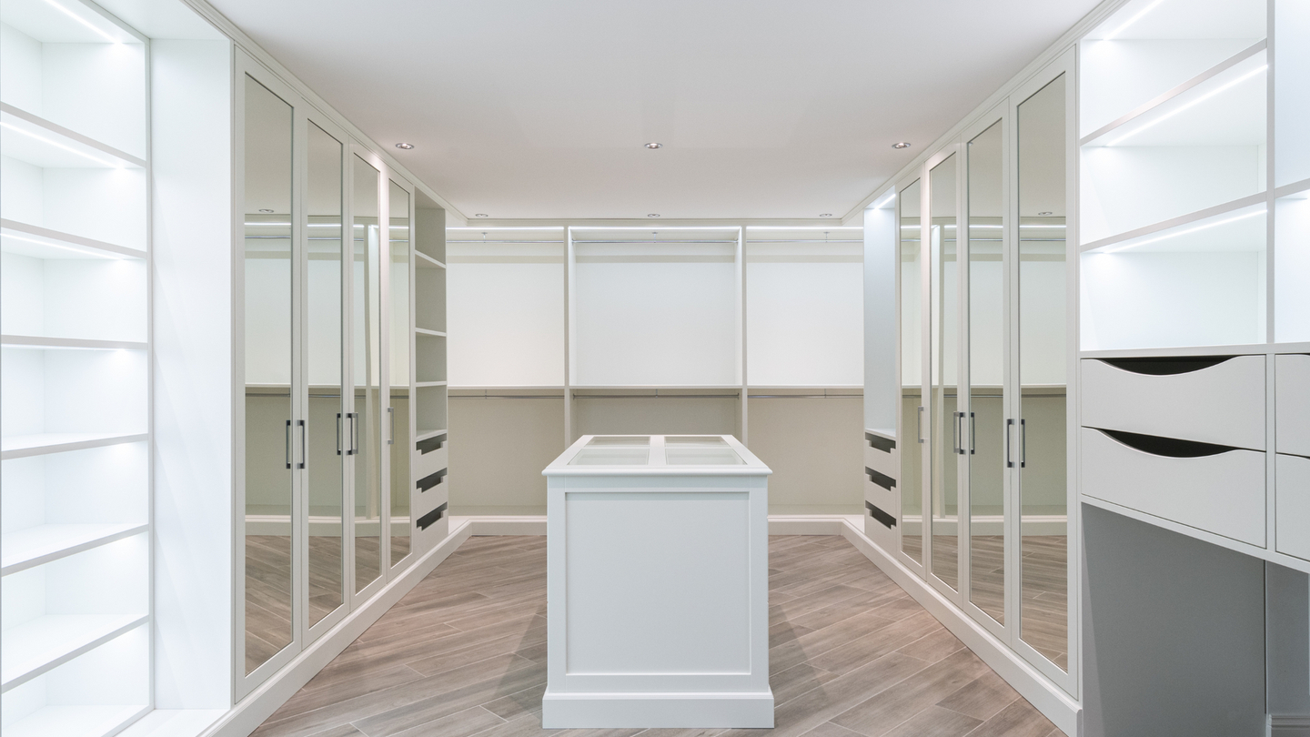 A large walk in closet with white cabinets and mirrored doors.