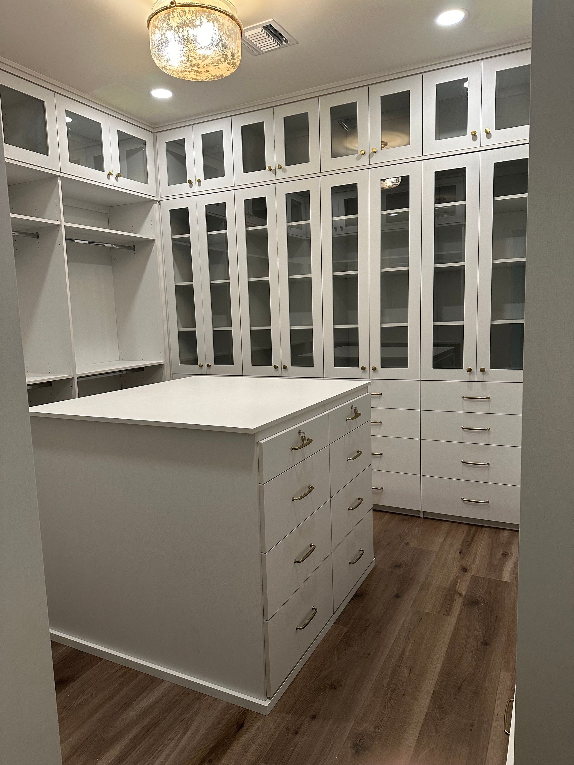 A walk in closet with lots of white cabinets and drawers and a large island in the middle.
