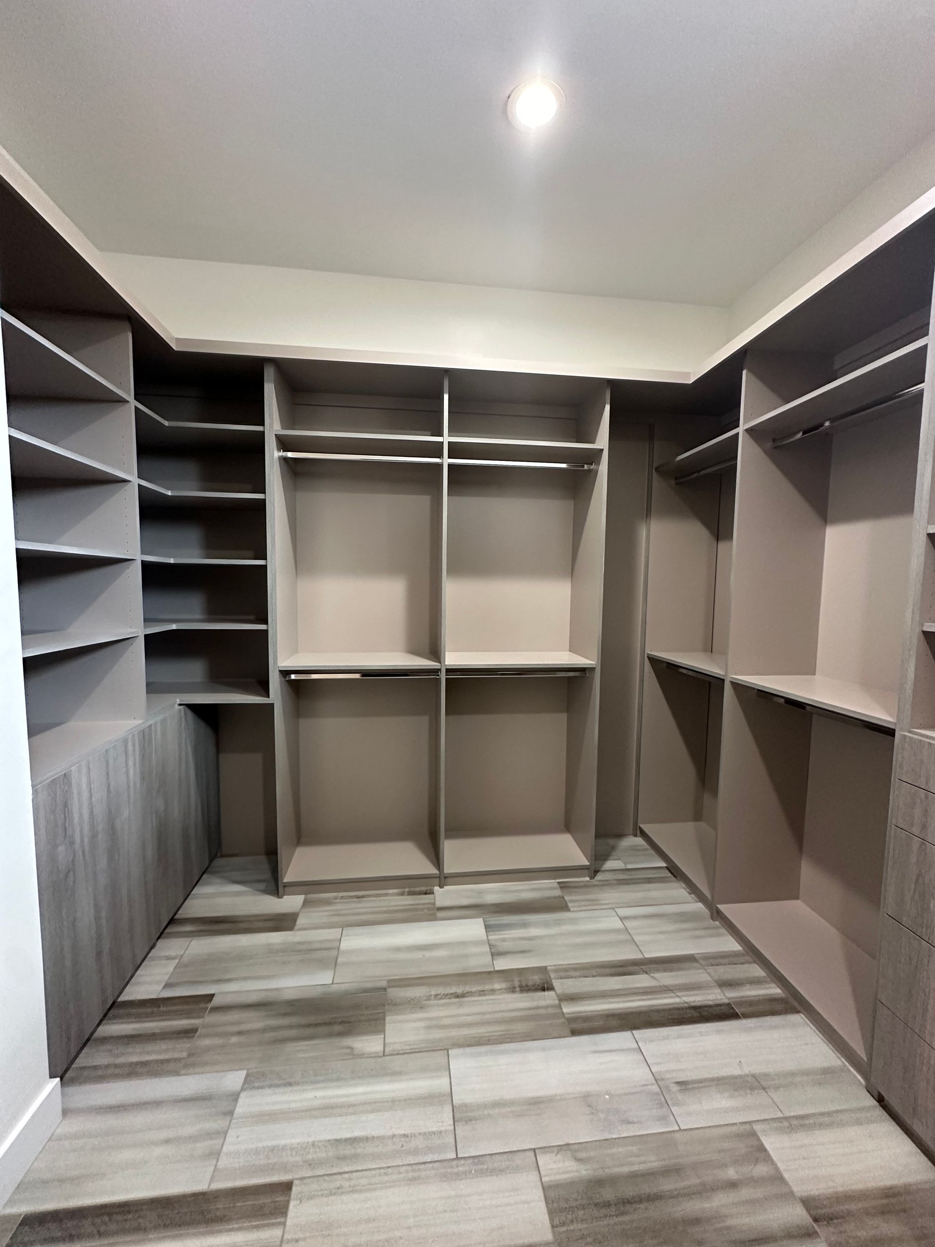 A large walk in closet with lots of shelves and a wooden floor.
