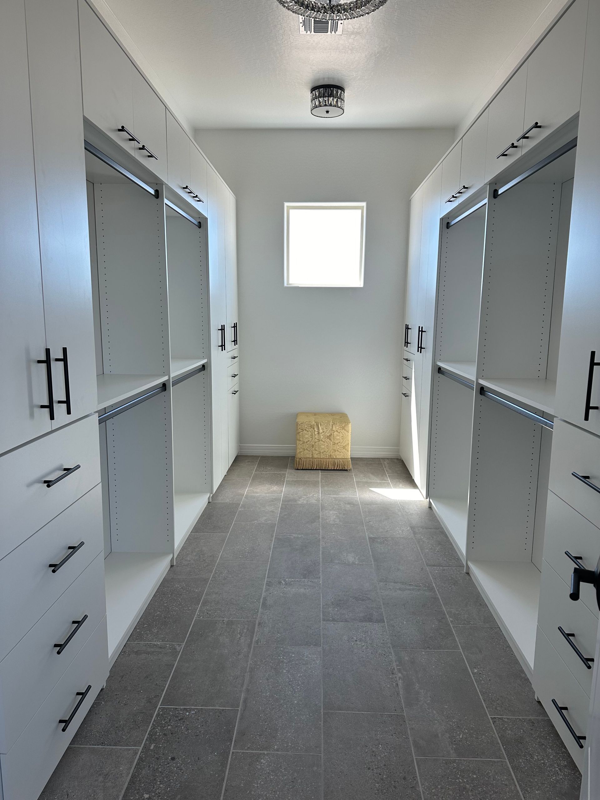 A walk in closet with white cabinets and drawers and a window.