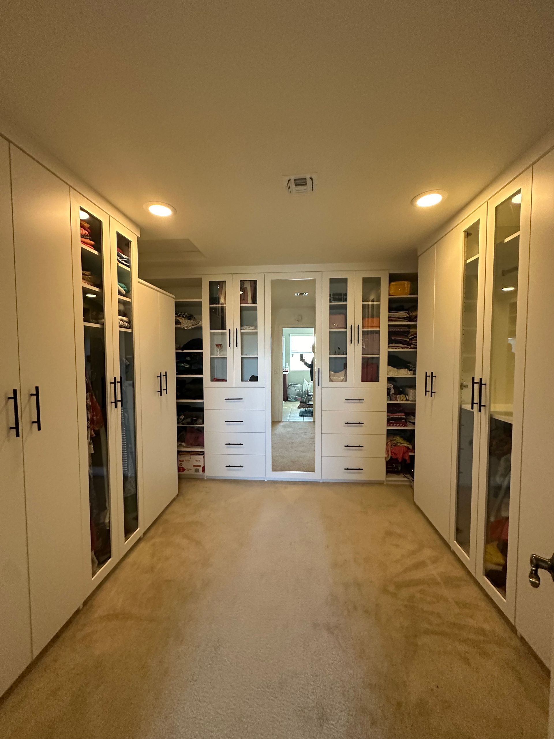 A walk in closet with lots of white cabinets and drawers