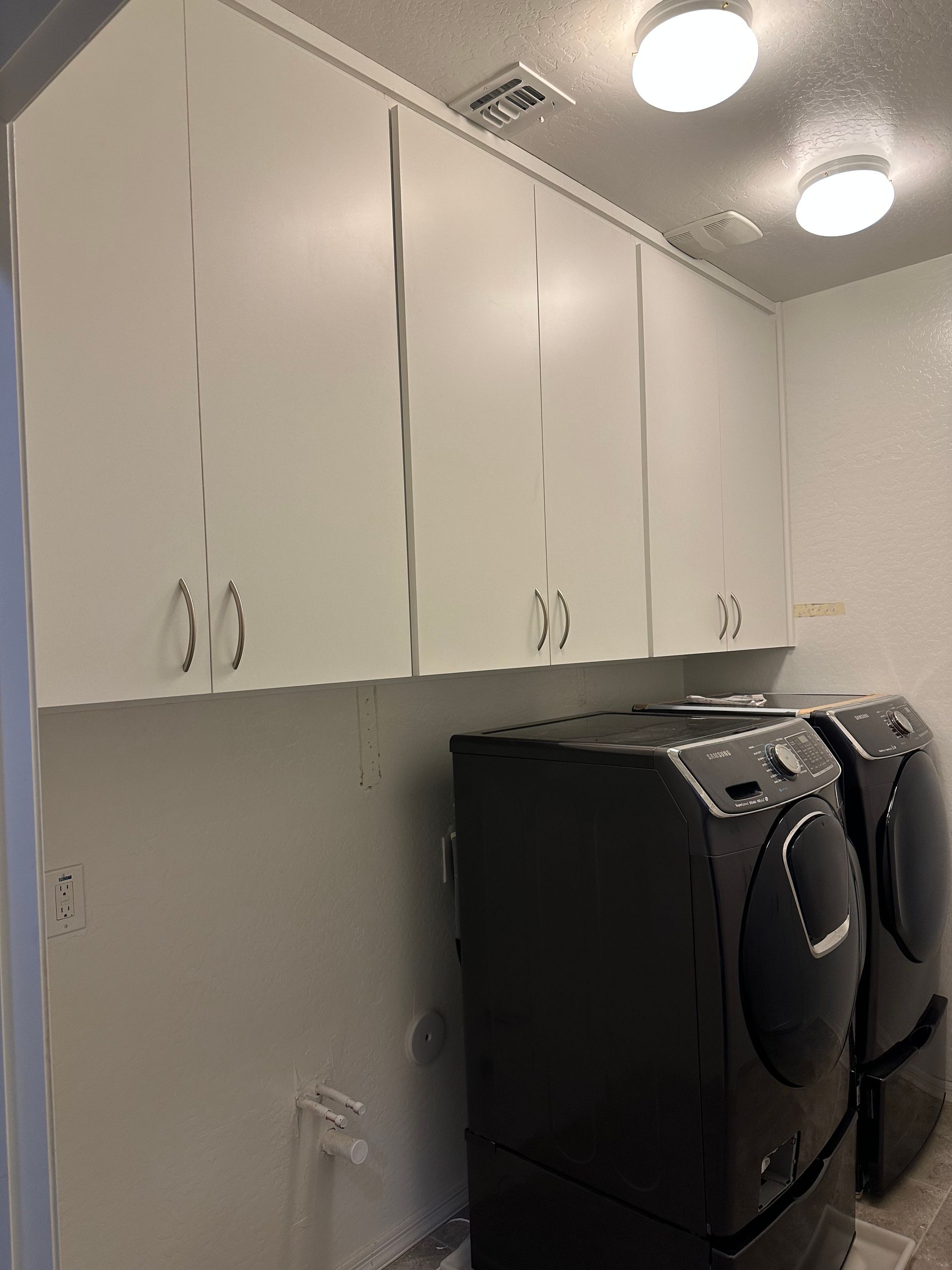 A laundry room with a washer and dryer and white cabinets.
