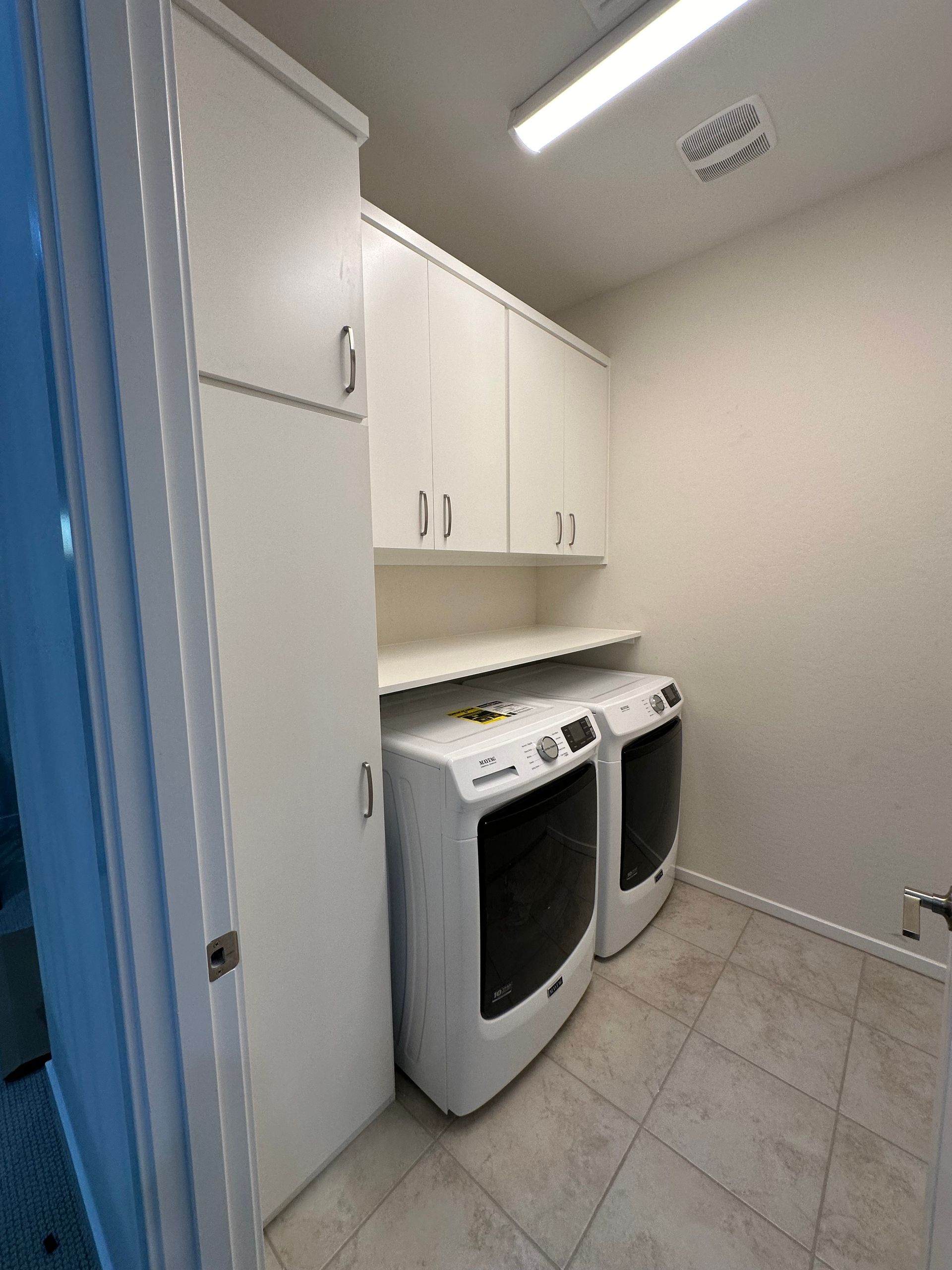 A laundry room with two washers and dryers and white cabinets.