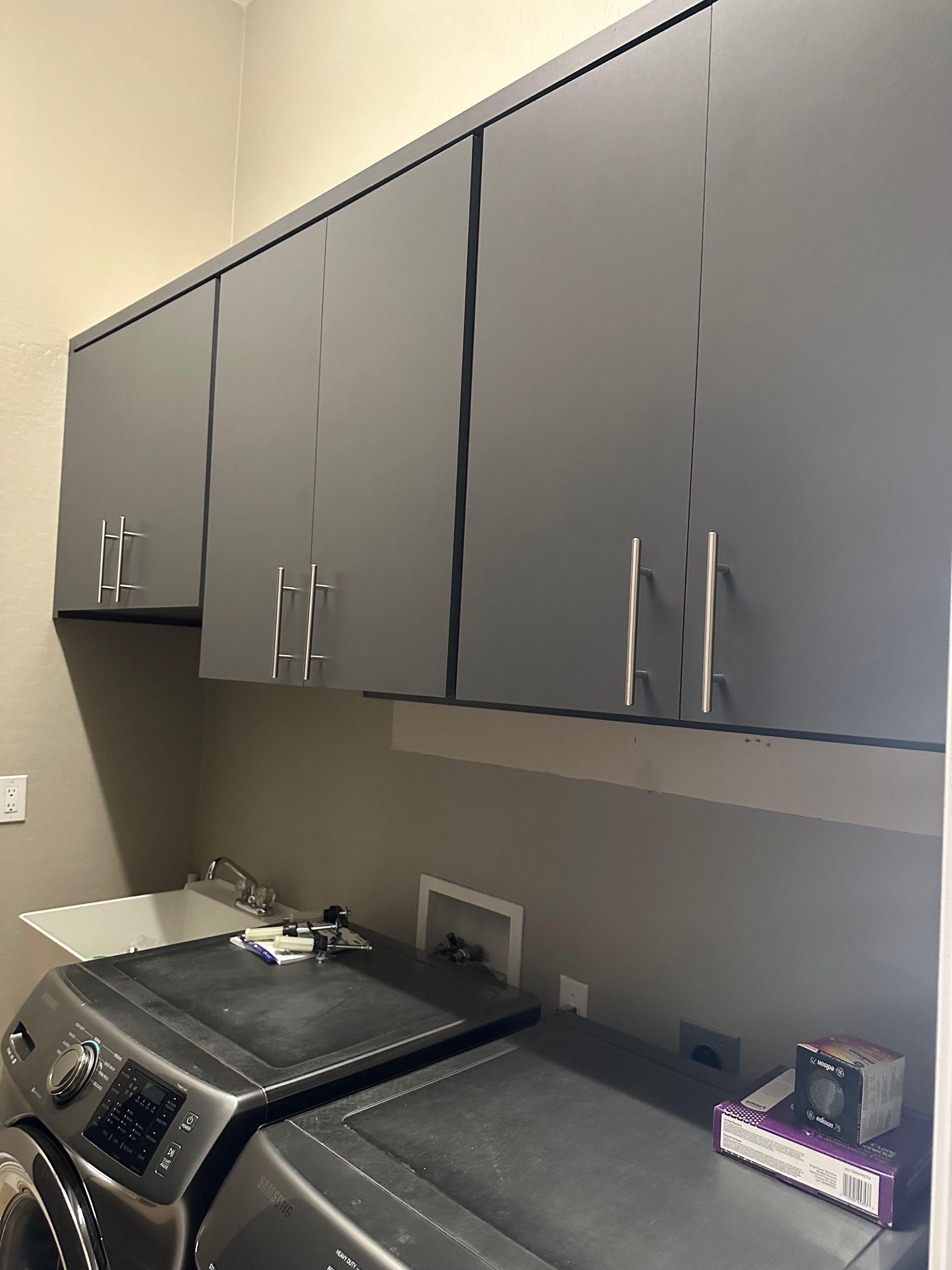 A laundry room with a washer and dryer and gray cabinets