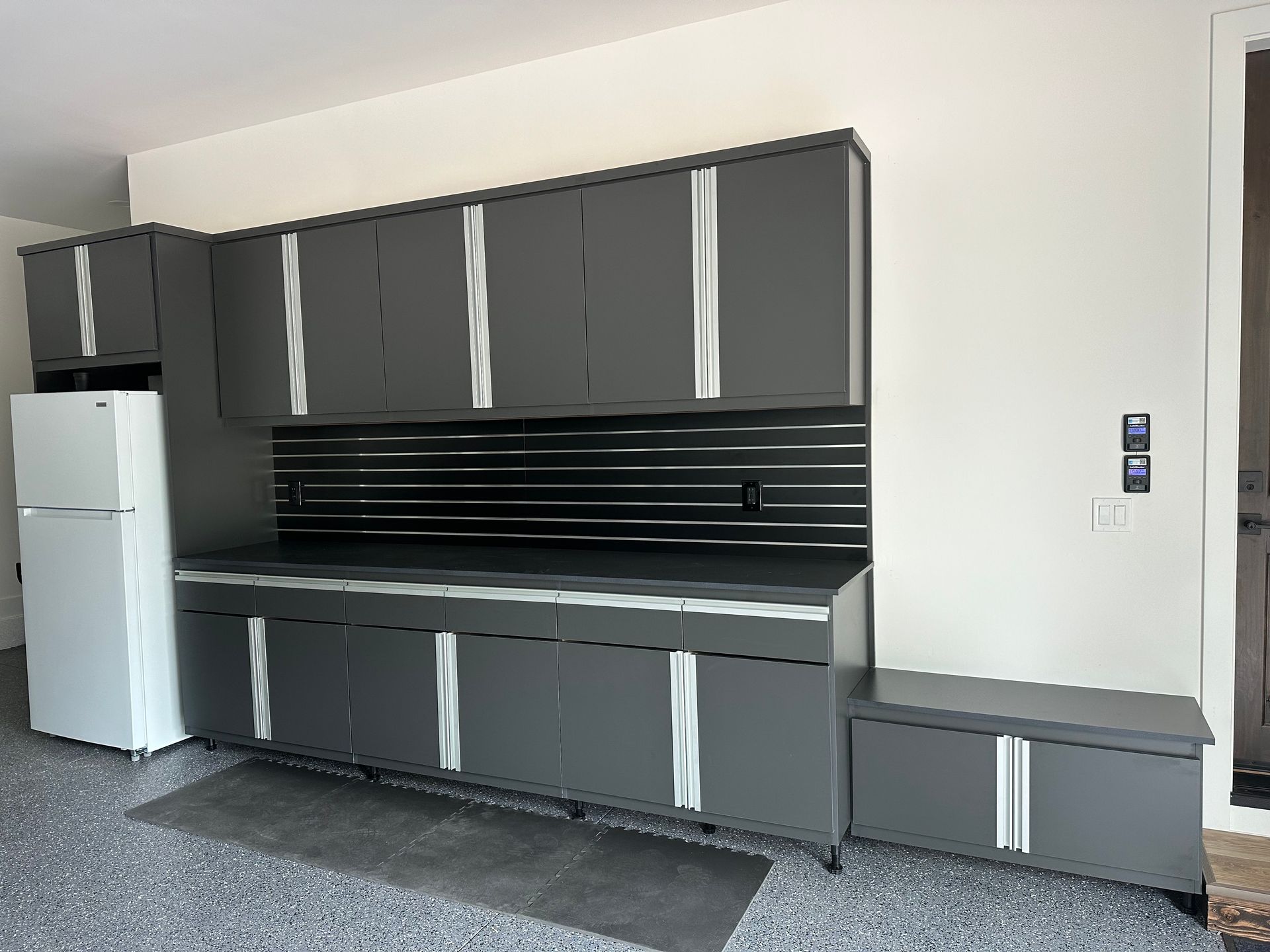A garage with gray cabinets and a white refrigerator.