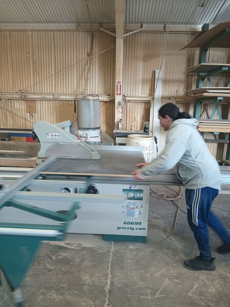 A man is standing in front of a table saw in a woodworking shop.