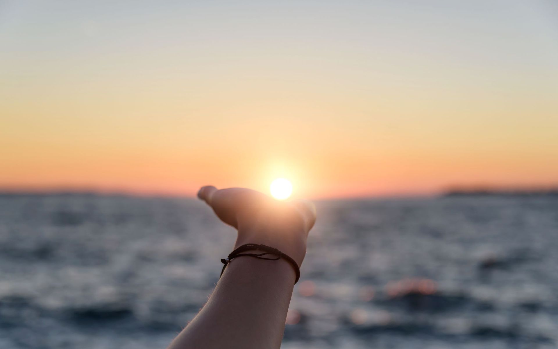 A Person is Holding the Sun in Their Hand in Front of the Ocean at Sunset — Becker Family Funerals In Forster, NSW