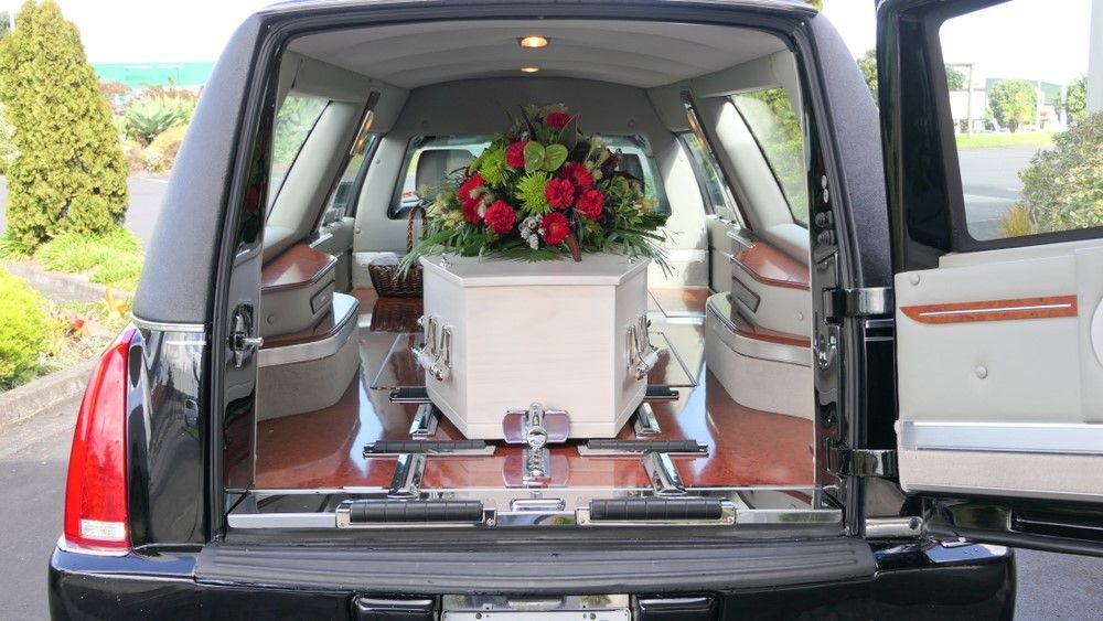 A White Coffin is Sitting in the Back of a Black Limousine — Becker Family Funerals In Taree, NSW