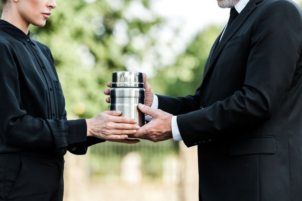 A Man in a Suit is Giving a Woman a Urn at a Funeral — Becker Family Funerals In Nelson Bay, NSW