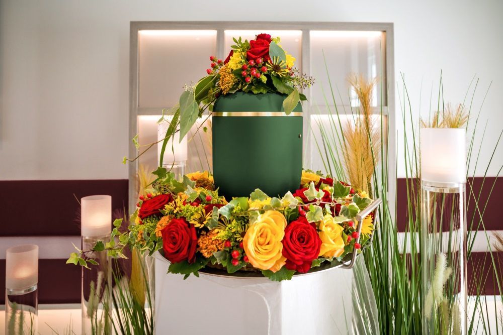 A Green Urn is Surrounded by Flowers in a Room — Becker Family Funerals In Taree, NSW