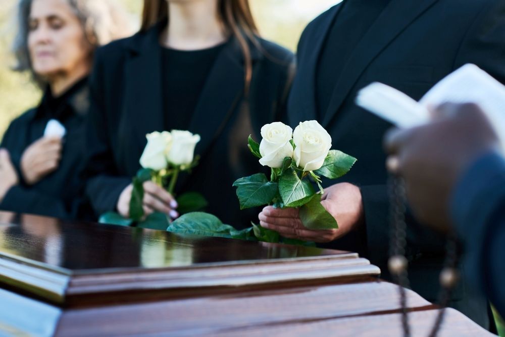 A Group of People Are Standing Around a Coffin at a Funeral — Becker Family Funerals In Taree, NSW