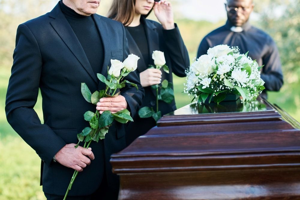 A Man and a Woman Are Standing Next to a Coffin at a Funeral — Becker Family Funerals In Nelson Bay, NSW
