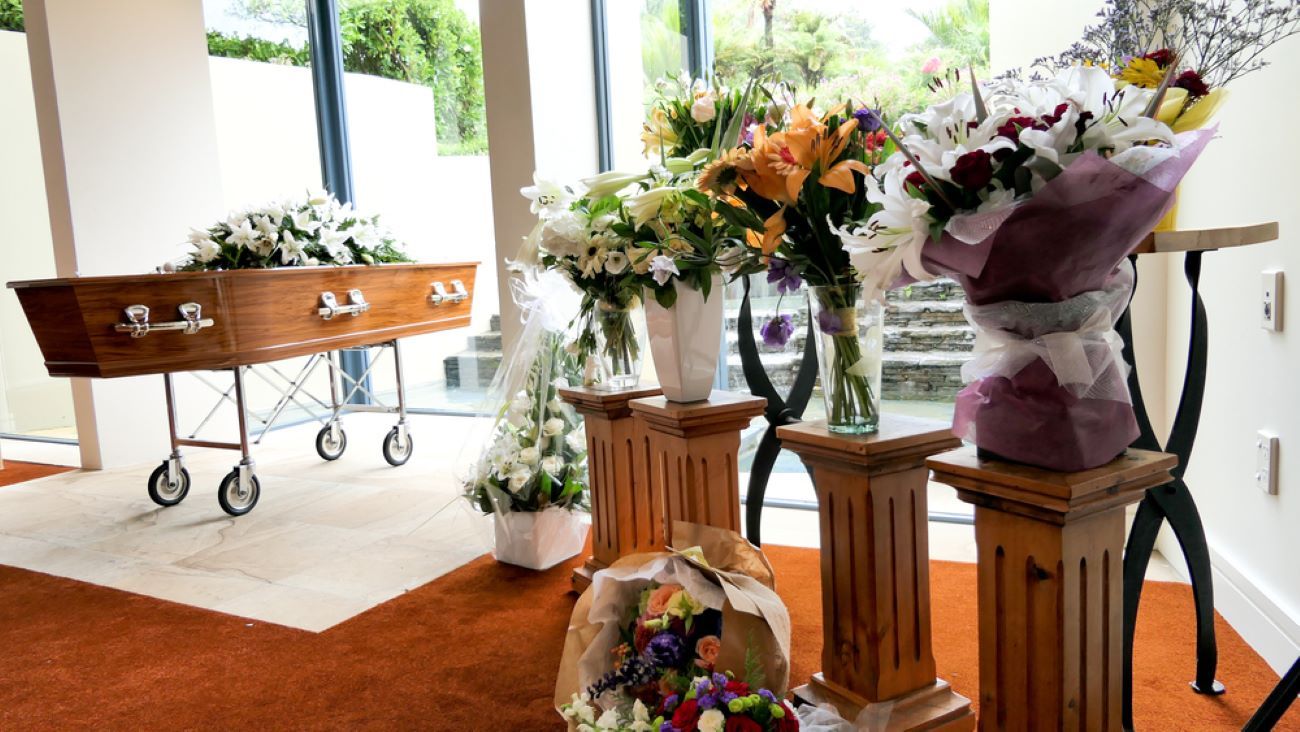 A Coffin is Sitting in a Room With Flowers on Pedestals — Becker Family Funerals In Forster, NSW