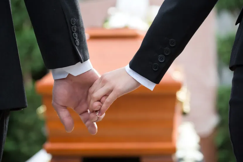 Due persone in abiti neri si tengono per mano durante una cerimonia nuziale davanti a una navata sfocata.